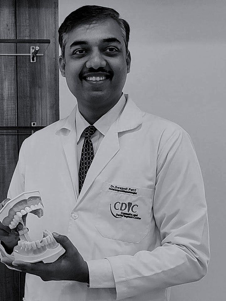 Dr. Swapnil B. Patil in a white coat, smiling, holding a model of the teeth.
